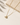 A gold chain necklace with a teardrop-shaped clear gemstone pendant in a gold bezel setting, styled on a light beige surface next to a textured stone block.