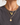 A close-up of a person wearing layered gold necklaces, including a starburst pendant, chain link necklace, and small charm pendants, paired with a dark gray t-shirt.